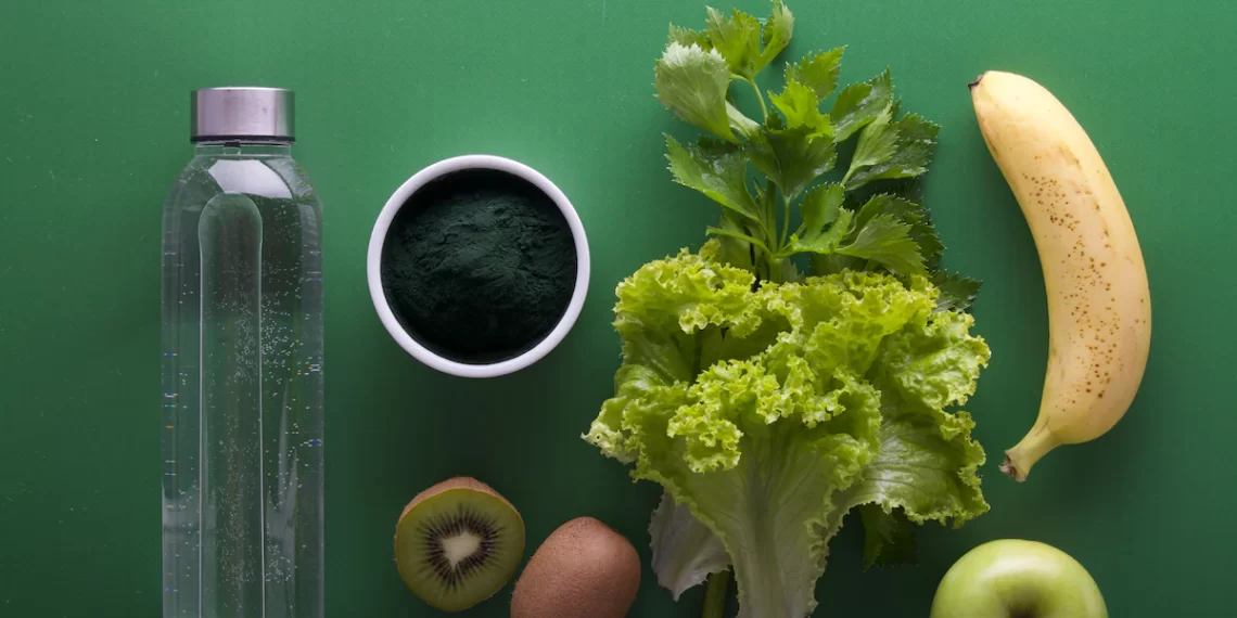 A bottle of water, kiwi, kiwifruit and green vegetables on a green background. Promoting healthy Diet and Nutrition.