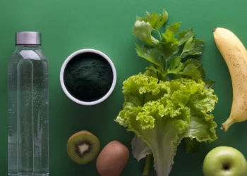 A bottle of water, kiwi, kiwifruit and green vegetables on a green background. Promoting healthy Diet and Nutrition.