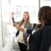 Two women engaged in workplace conflict standing in front of a whiteboard in an office.